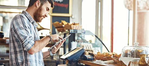 Man using tablet behind the counter of a coffee shop